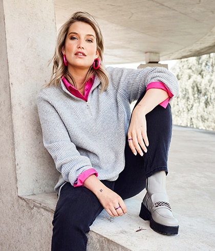 The model poses in a grey sweater and a pink blouse