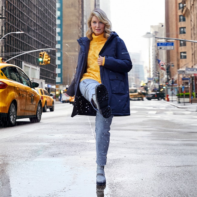 The model wears a yellow sweater and a blue winter coat.