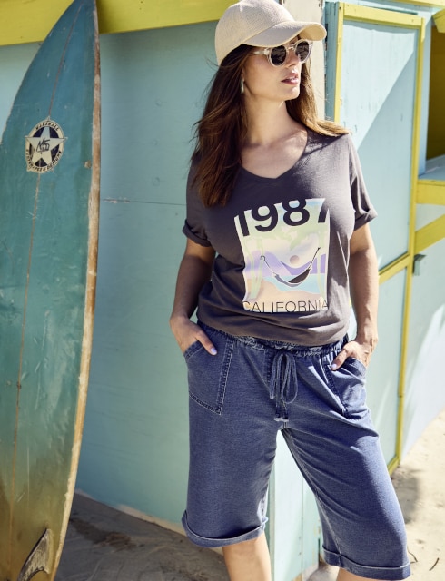 Model mit Sonnenbrille und Cap posiert vor einer blauen Hütte