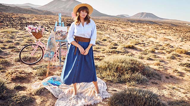 The model wears a blouse and jeans skirt and has a straw hat on