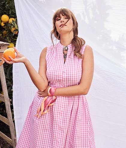 The model poses in a pink dress while she holds a orange in her hand