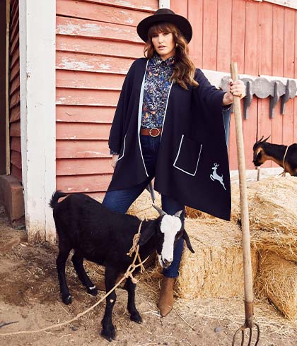 The model poses next to a goat in a dark blue cape   
