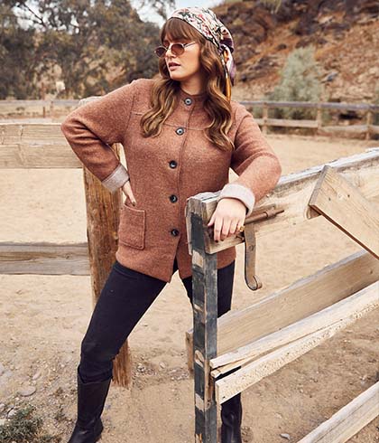 The model poses on the fence and wears a brown cardigan 
