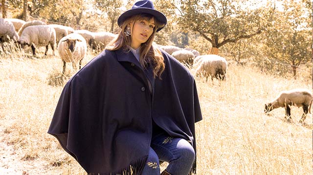 The model wears a large blue cape 