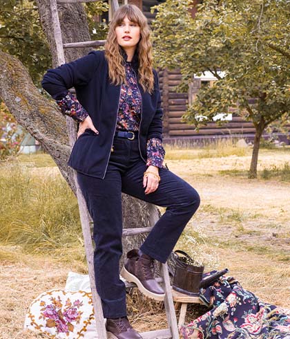 The model is sitting on a ladder leaning against a tree and wears a blue jacket. 