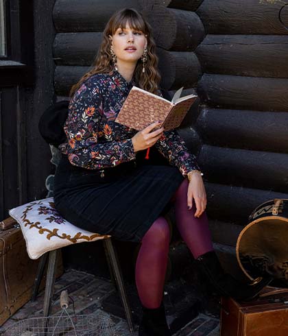 The model poses sitting and rummaging through a book 