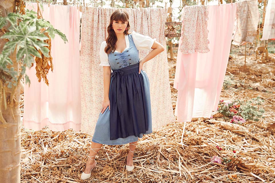 The model is wearing a light blue dirndl with a dark blue apron