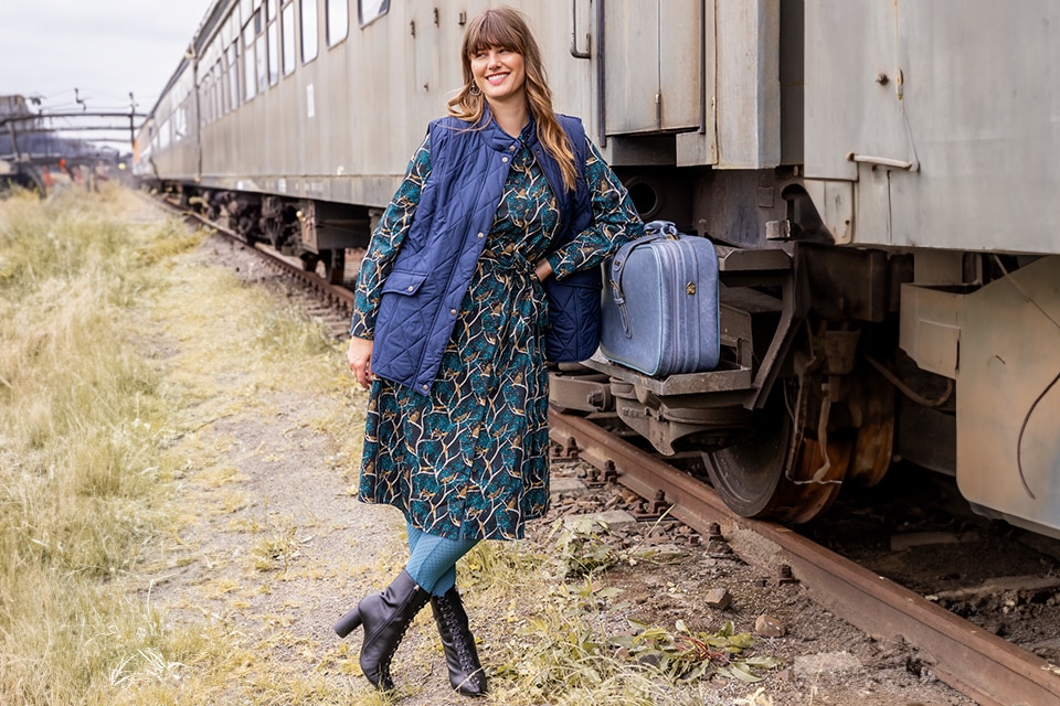 The model is wearing a knee-length, flowered skirt and a dark blue quilted vest 
