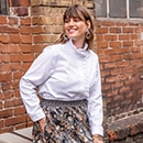 The model is wearing a white blouse with appliqués