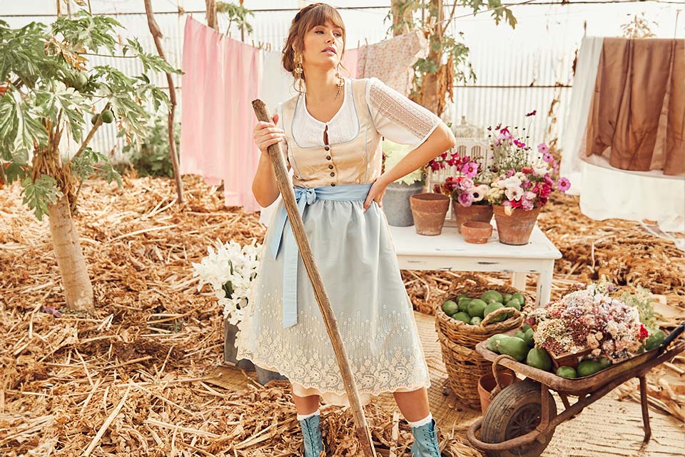 The model is wearing a beige dirndl with a light blue apron