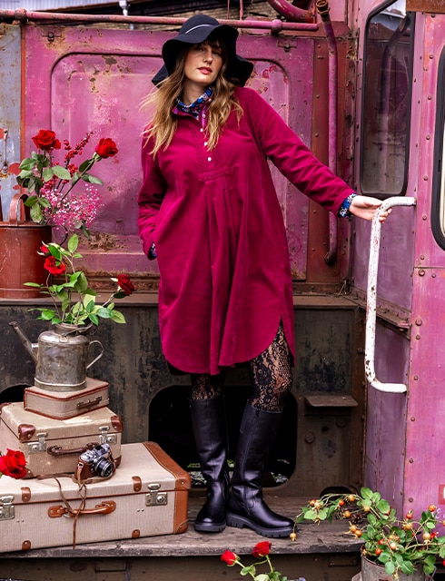 The model poses by a pink train carriage and wears a pink corduroy dress 
