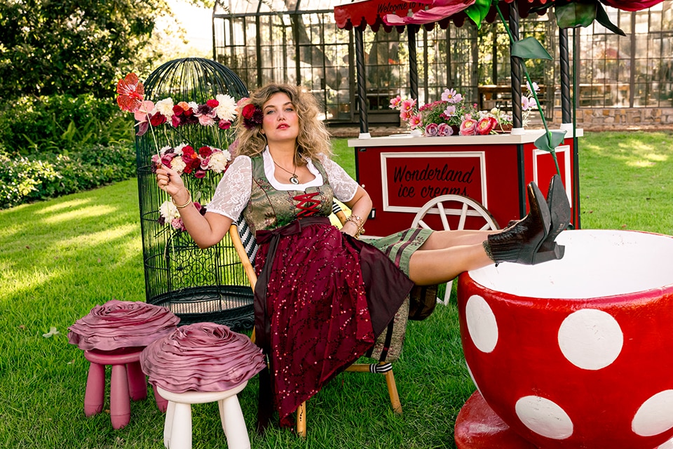 The model poses in a green and green dirndl and wears red wellies