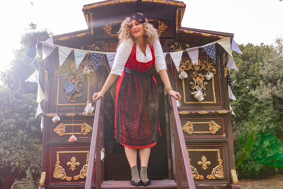 The model is wearing a light blue dirndl with a dark blue apron