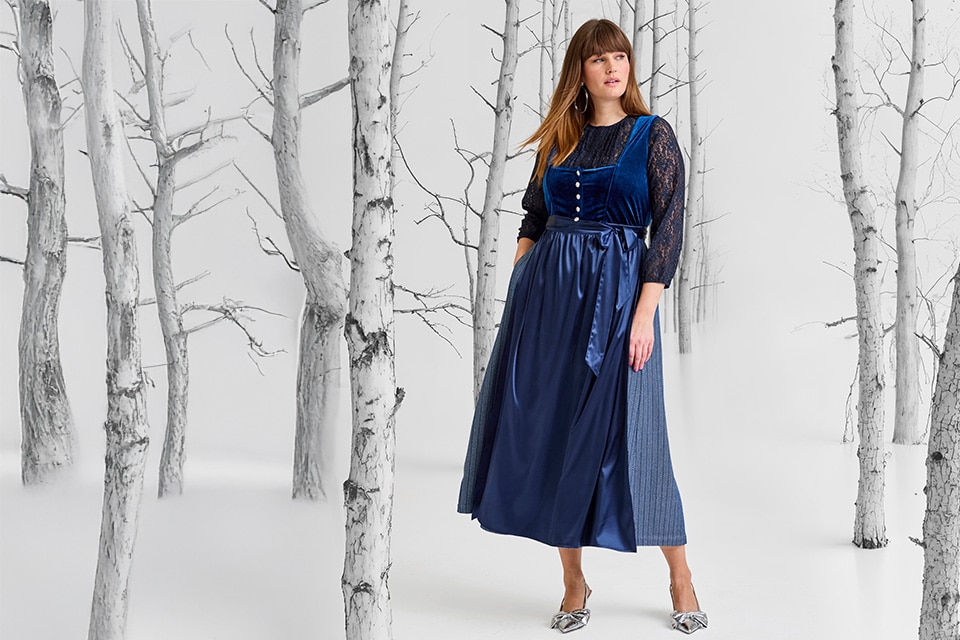 The model is wearing a light blue dirndl with a dark blue apron