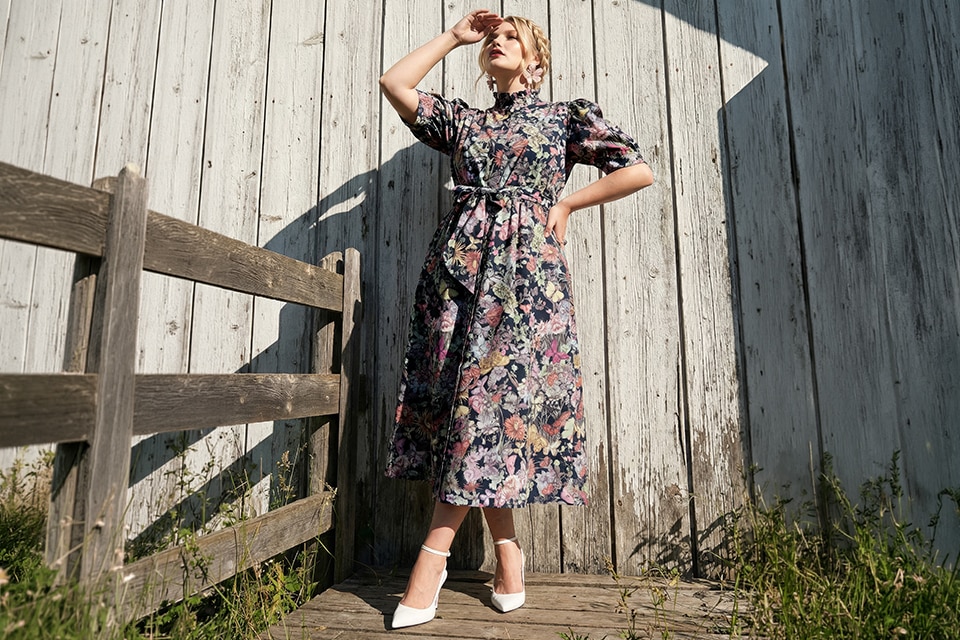 The model wears a black dress with colorful flowers.