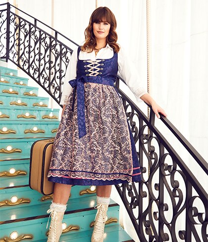 Woman in a dark blue dirndl posing on a staircase
