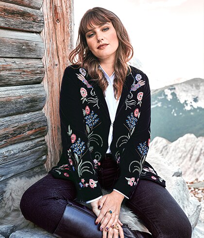 Woman with flowered velvet blazer sitting on stones