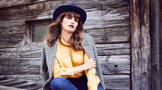 Woman with hat and yellow blouse posing on a wooden bench