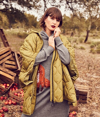 Model posiert vor Holzkisten in einem braunen Mantel