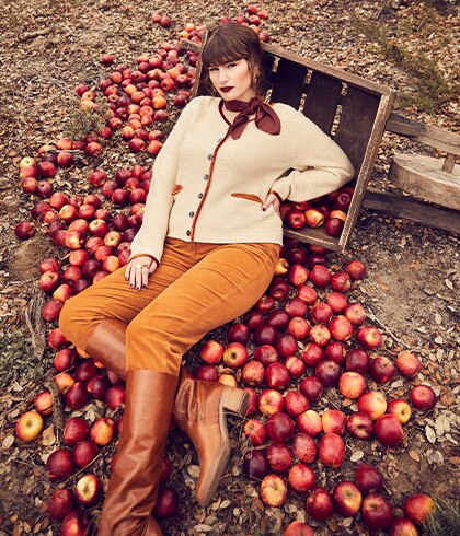 Model in a beige cardigan lies on a pile of apples