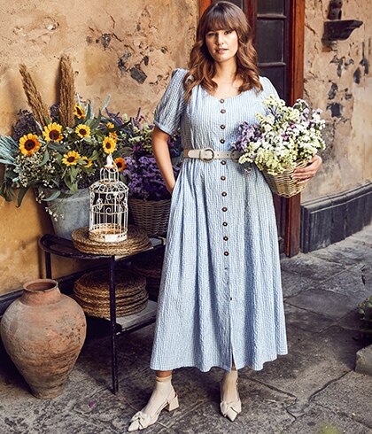 Woman with a shirt dress on and a plant pot with flowers in her hand