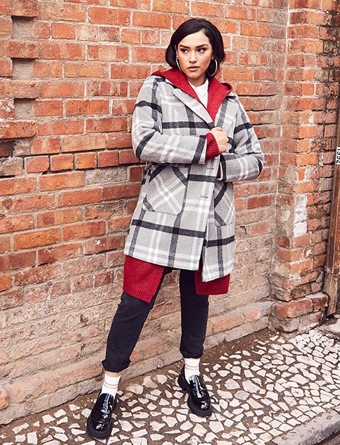 Standing woman in a checked coat standing in front of a house wall