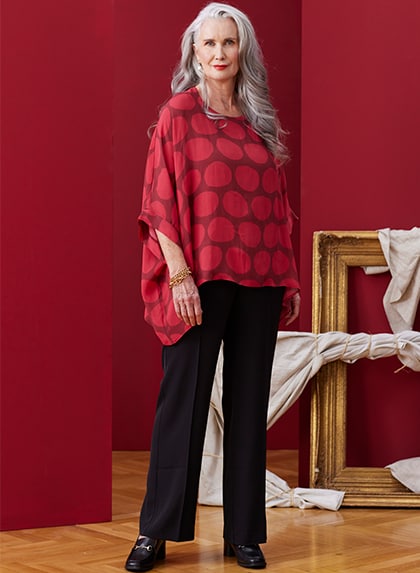 Woman standing in front of a red wall with a red blouse and black cloth trousers