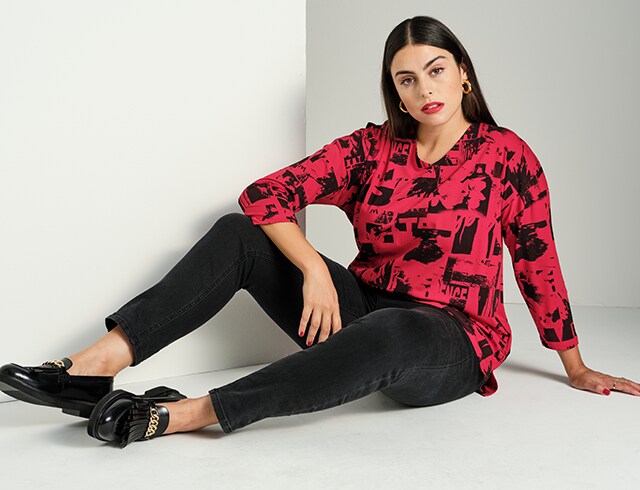 Model sitting on the floor in a black and red patterned top