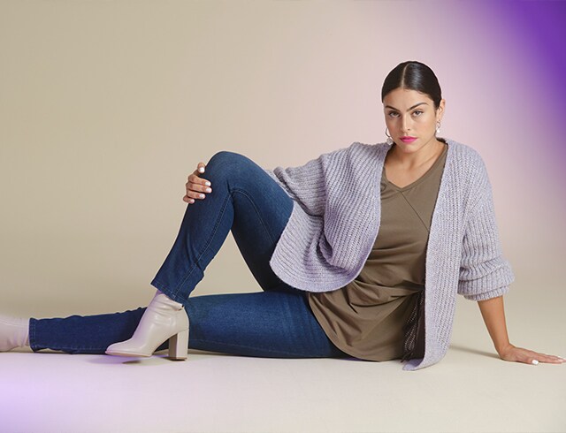 Woman in blue jeans and grey knitted jacket poses on the floor