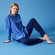Model in blue blouse and blue trousers poses sitting on blue floor