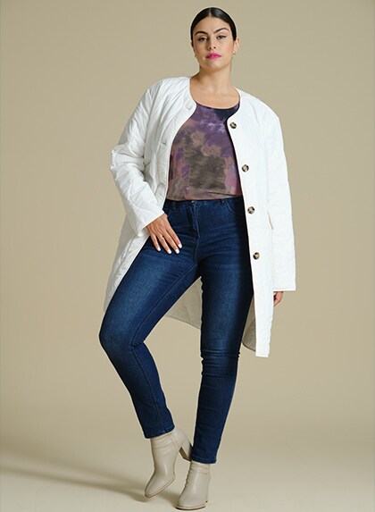 Model in white jacket and blue jeans poses in front of a white background