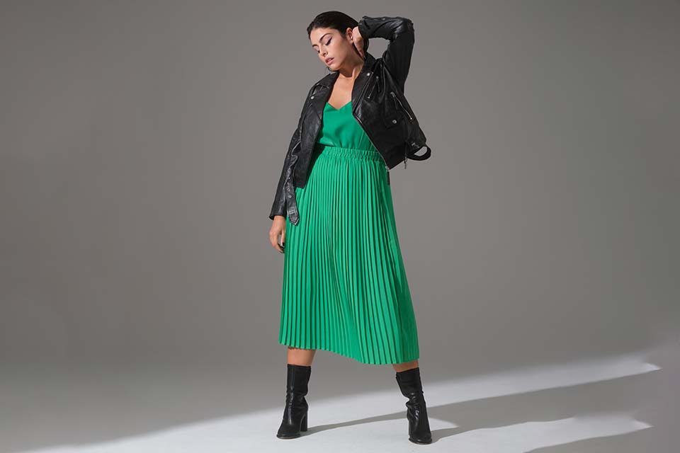 A dark-haired woman poses in a green dress and a black leather jacket