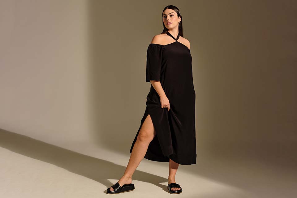 Ein Model posiert mit einem langen schwarzen Kleid mit Neckholder