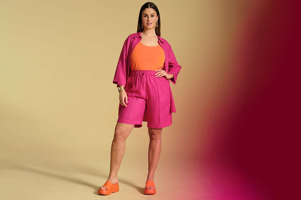 Ein Model trägt eine pinke kurze Hose, ein pinkes Hemd und ein orangenes Top