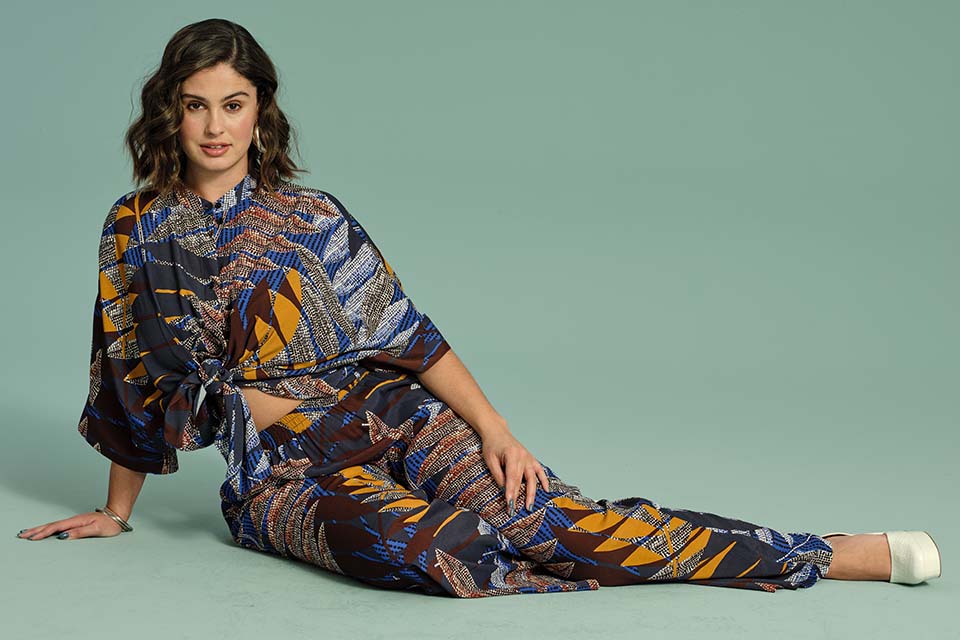 Model poses on the floor in a colourful blouse and trousers