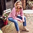 Woman posing on chair in jeans and pink sweater