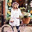 Woman posing by a bike in a white blouse with blue dots 