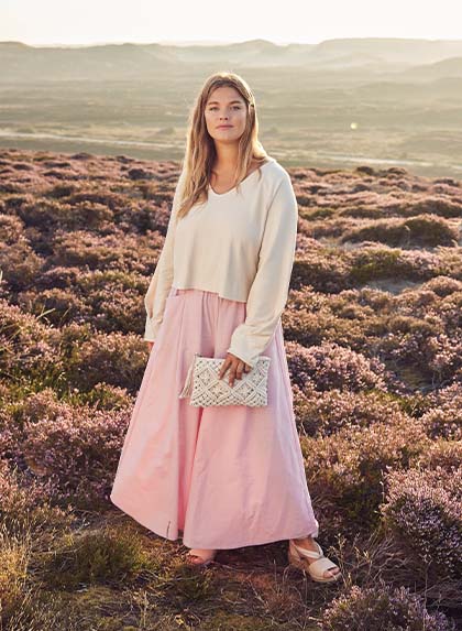 The model stands in a flower meadow and wears pink trousers 


