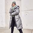 The model poses in a grey quilted coat 
