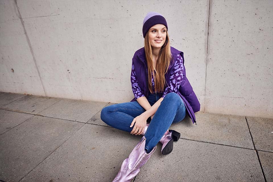 The model poses in purple trousers and a long sweat jacket in front of a taxi 