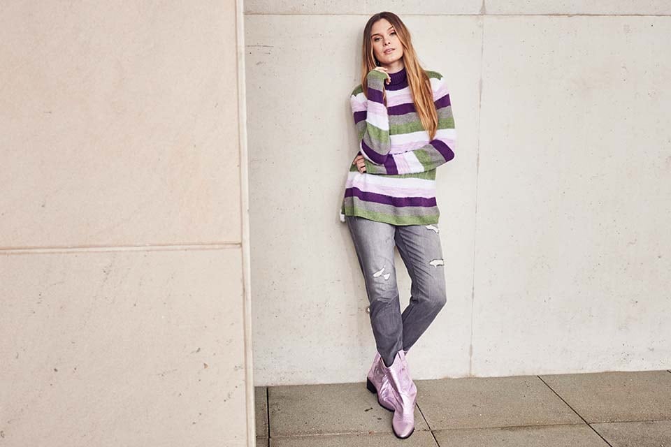 The model poses sitting in a patterned shirt, a purple waistcoat and a pair of jeans. She combines this with a purple cap  