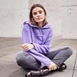 The model poses sitting in a purple jumper and grey jeans  