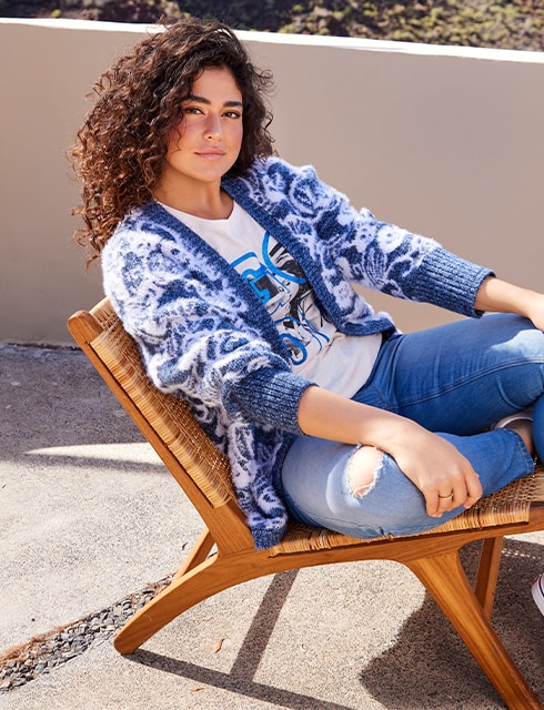 The model poses in a blue and white cardigan on a chair 